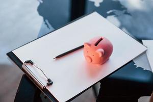 Close up view of pink piggy bank that lying on the white document on table photo