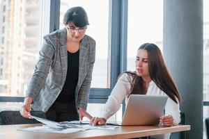 Using laptop. Two women in formal clothes is indoors in the modern office works together photo