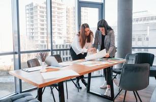 Standing and talking. Two women in formal clothes is indoors in the modern office works together photo