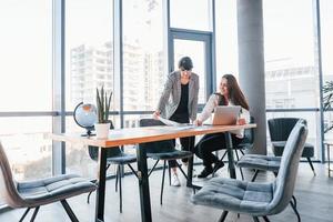 Using laptop. Two women in formal clothes is indoors in the modern office works together photo