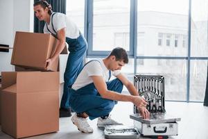 Uses tools from case. Two young movers in blue uniform working indoors in the room photo