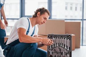 Uses tools from case. Two young movers in blue uniform working indoors in the room photo