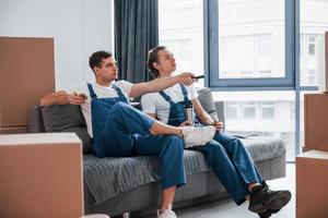 Sitting on the sofa. Tired and taking break. Two young movers in blue uniform working indoors in the room photo