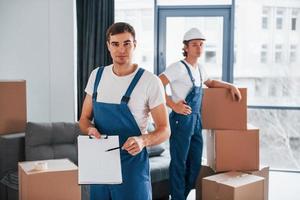 Document to sign. Two young movers in blue uniform working indoors in the room photo