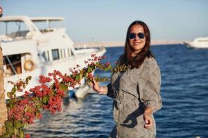 Cheerful mature woman standing against white yacht on the sea photo