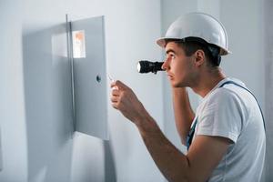 Young male electrician in white hard hat works indoors in the room photo