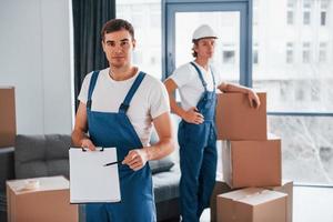 Document to sign. Two young movers in blue uniform working indoors in the room photo