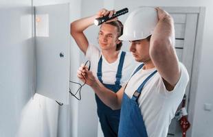 dos jóvenes electricistas trabajan juntos en interiores. usando linterna foto