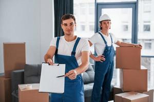 Document to sign. Two young movers in blue uniform working indoors in the room photo