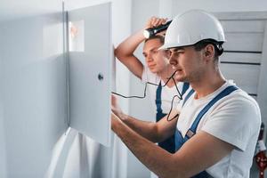 dos jóvenes electricistas trabajan juntos en interiores. usando linterna foto