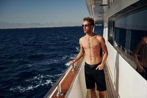 Warm weather. Young male tourist is on the yacht on the sea. Conception of vacation photo