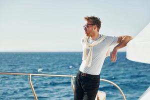 Warm weather. Young male tourist is on the yacht on the sea. Conception of vacation photo