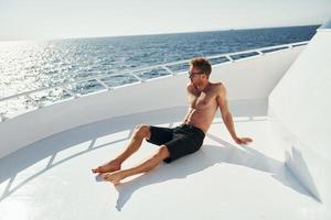 In sunglasses. Young male tourist is on the yacht on the sea. Conception of vacation photo