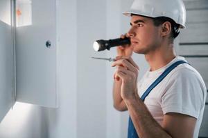 un joven electricista con sombrero duro blanco trabaja en el interior de la habitación foto