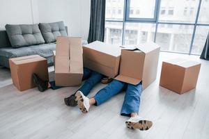 Two young male movers in blue uniform lying down on the floor with boxes photo