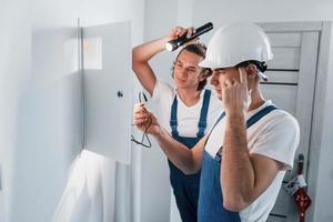 dos jóvenes electricistas trabajan juntos en interiores. usando linterna foto