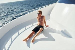 In sunglasses. Young male tourist is on the yacht on the sea. Conception of vacation photo