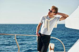 Warm weather. Young male tourist is on the yacht on the sea. Conception of vacation photo