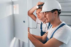 dos jóvenes electricistas trabajan juntos en interiores. usando linterna foto