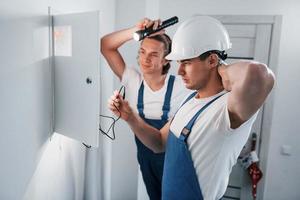 dos jóvenes electricistas trabajan juntos en interiores. usando linterna foto