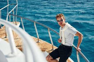 Posing for a camera. Young male tourist is on the yacht on the sea. Conception of vacation photo