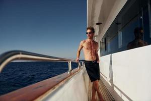 Warm weather. Young male tourist is on the yacht on the sea. Conception of vacation photo