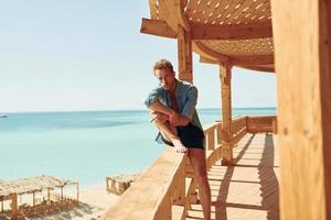 Wooden building. Young european man have vacation and enjoying free time on the beach of sea photo