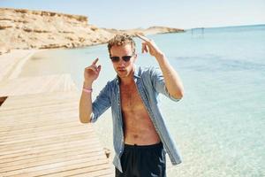 In sunglasses. Young european man have vacation and enjoying free time on the beach of sea photo