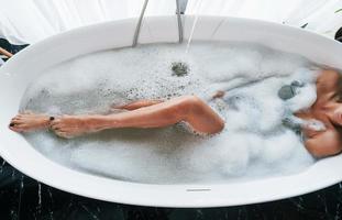 Particle view of legs. Beautiful young woman have free time at home in the bath photo