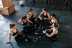 Sitting on floor. Group of young sportive people have crossfit day indoors in gym photo