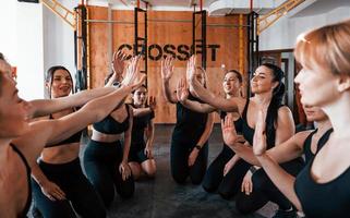 Sitting on floor. Group of young sportive people have crossfit day indoors in gym photo