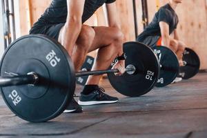 By using heavy weights. Group of young sportive people have crossfit day indoors in gym photo