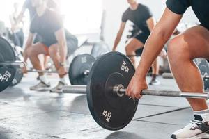 By using heavy weights. Group of young sportive people have crossfit day indoors in gym photo