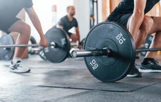 By using heavy weights. Group of young sportive people have crossfit day indoors in gym photo