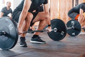 By using heavy weights. Group of young sportive people have crossfit day indoors in gym photo