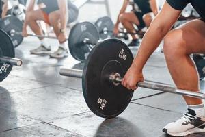 By using heavy weights. Group of young sportive people have crossfit day indoors in gym photo