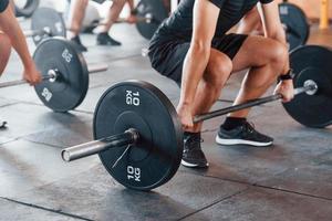 mediante el uso de pesos pesados. grupo de jóvenes deportistas tienen un día de crossfit en el interior del gimnasio foto