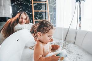 Young mother helps her son and daughter. Two kids washing in the bath photo