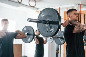 By using heavy weights. Group of young sportive people have crossfit day indoors in gym photo