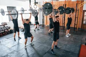 Together with barbells. Group of young sportive people have crossfit day indoors in gym photo