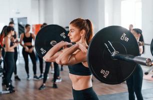 sentadillas con barra. grupo de jóvenes deportistas tienen un día de crossfit en el interior del gimnasio foto