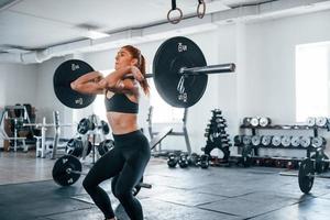 Young fitness woman with slim type of body doing exercises by using barbell photo