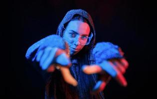 Does gestures by hands. Portrait of young girl that is in eyeglasses in blue neon lighting photo