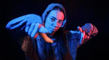 Does gestures by hands. Portrait of young girl that is in eyeglasses in blue neon lighting photo