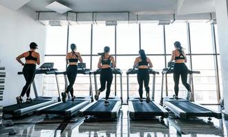 Running on a treadmill. Group of young sportive people have crossfit day indoors in gym photo