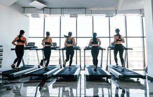 Running on a treadmill. Group of young sportive people have crossfit day indoors in gym photo