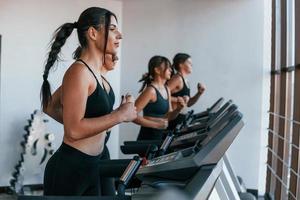 Running on a treadmill. Group of young sportive people have crossfit day indoors in gym photo