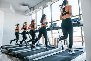 Running on a treadmill. Group of young sportive people have crossfit day indoors in gym photo