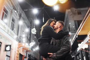 abrazándose unos a otros. feliz pareja multirracial juntos al aire libre en la ciudad celebrando el año nuevo foto