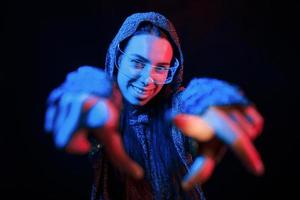 Does gestures by hands. Portrait of young girl that is in eyeglasses in blue neon lighting photo